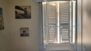 A bedroom with a bed, a radiator, a window with shutters, and wall art.