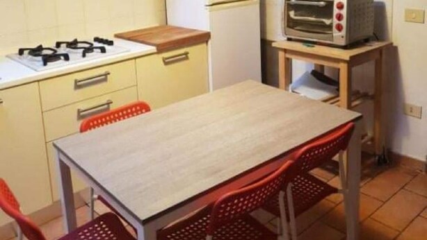 Een compacte keuken met een gasfornuis, een kleine koelkast, een toasteroven en een eettafel met rode stoelen.