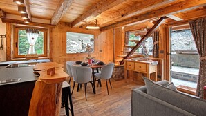 Ein Holzblockhaus-Interieur mit Esstisch, Stühlen, einer Couch und einer Küchenzeile.
