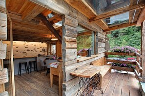 Un intérieur rustique en bois, avec un bar, des tabourets et une grande fenêtre donnant sur un espace verdoyant.