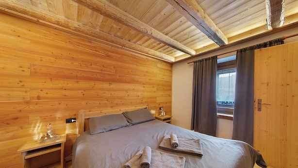 Una habitación con paneles de madera, una cama, una mesita de noche y un ventanal con cortinas.