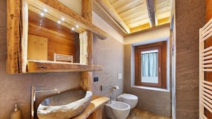 Un baño rústico con lavamanos de piedra, vigas de madera y una ventana.