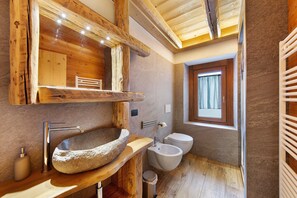 Un baño rústico con lavamanos de piedra, vigas de madera y una ventana.