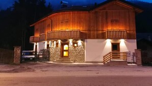 A two-story wooden building with a stone facade, a balcony, and a staircase leading to the entrance. - Apartment 'Ciariè' with Mountain View (Auronzo di Cadore)
