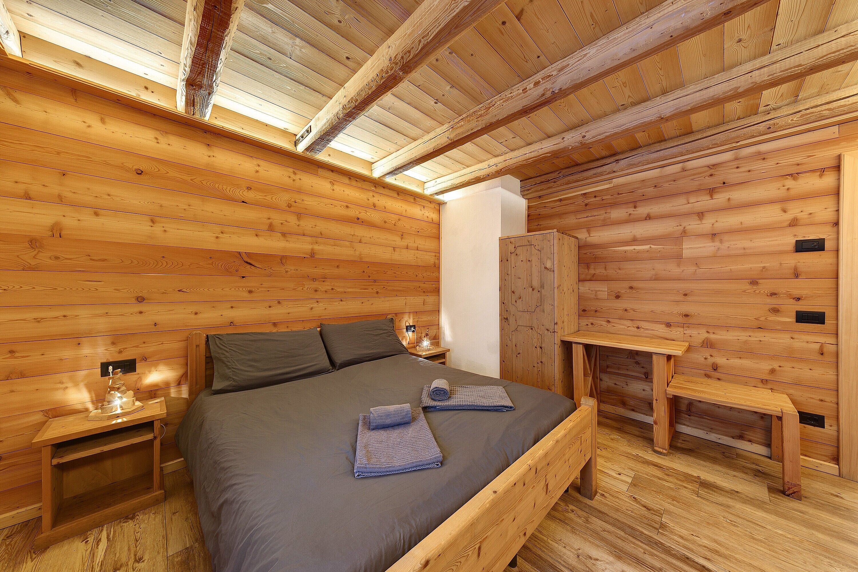 A wooden cabin room with a bed, nightstands, a bench, and a wardrobe.