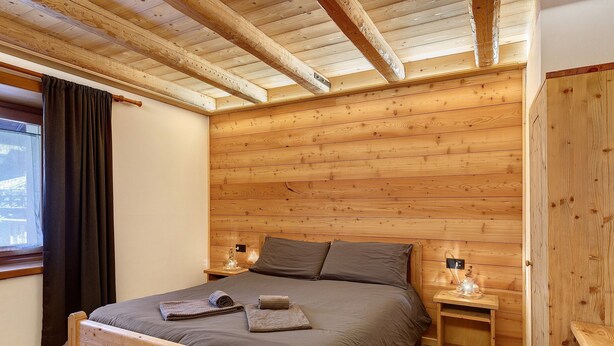 A wooden-paneled bedroom with a bed, nightstands, and a window with curtains. - Apartment 'Ciariè' with Mountain View (Auronzo di Cadore)