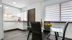 A modern kitchen with white cabinets, a glass dining table, and a door with blinds.
