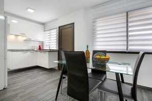 Una cocina moderna con armarios blancos, una mesa de comedor de vidrio y una puerta con persianas.