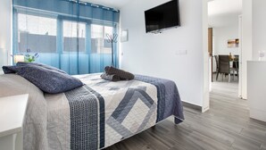 A bedroom with a bed, a TV, a window with curtains, and a door leading to another room.