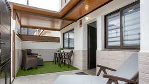 A modern outdoor patio with a lounge chair, a small table, and a seating area with chairs.