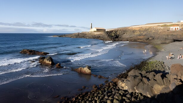 A coastal landscape with a lighthouse, rocky shoreline, and a sandy beach.