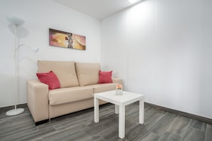 Une pièce moderne avec un canapé beige, une table basse blanche, un lampadaire et un tableau au mur.
