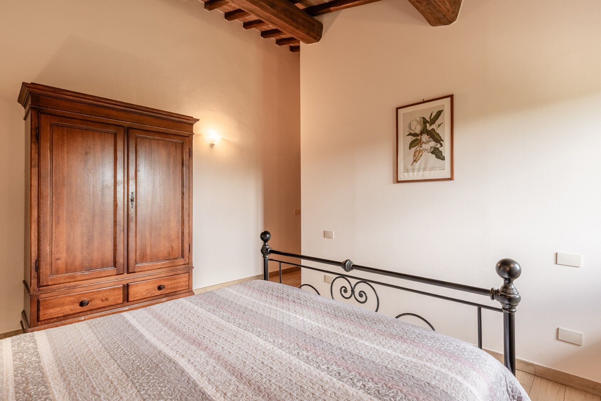 A bedroom with a bed, wooden wardrobe, and a wall-mounted light fixture.