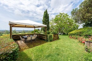 A covered patio with a table and chairs, surrounded by a well-maintained garden and a view of the countryside. - Apartment 'Lo Stornello' with Shared Pool, Wi-Fi and Air Conditioning (Fucecchio)