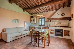 Une cuisine chaleureuse avec une table à manger, des chaises en bois, un canapé et un mur recouvert de carreaux.