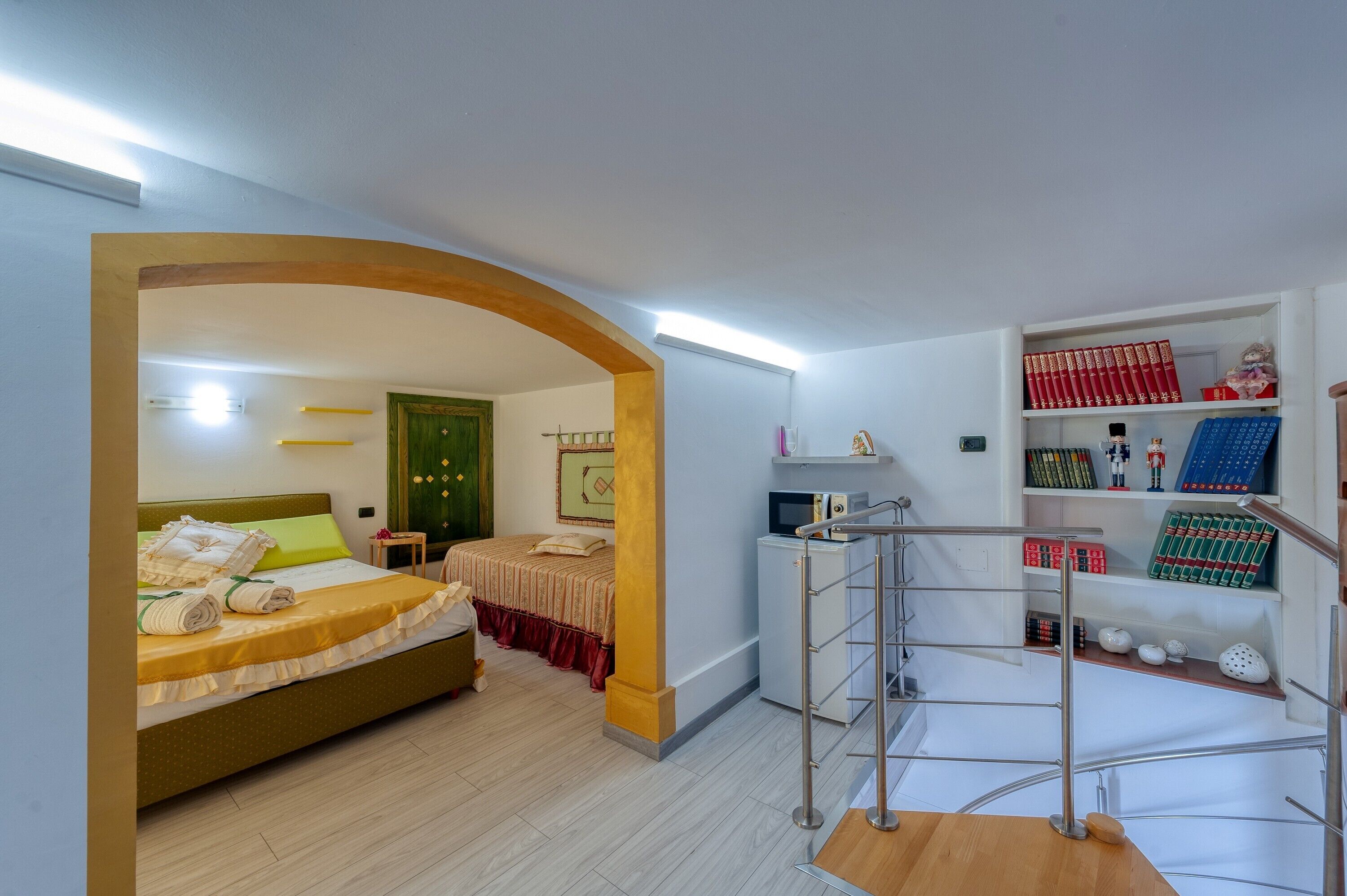 A hotel room with a bed, a desk, a bookshelf, and a staircase.