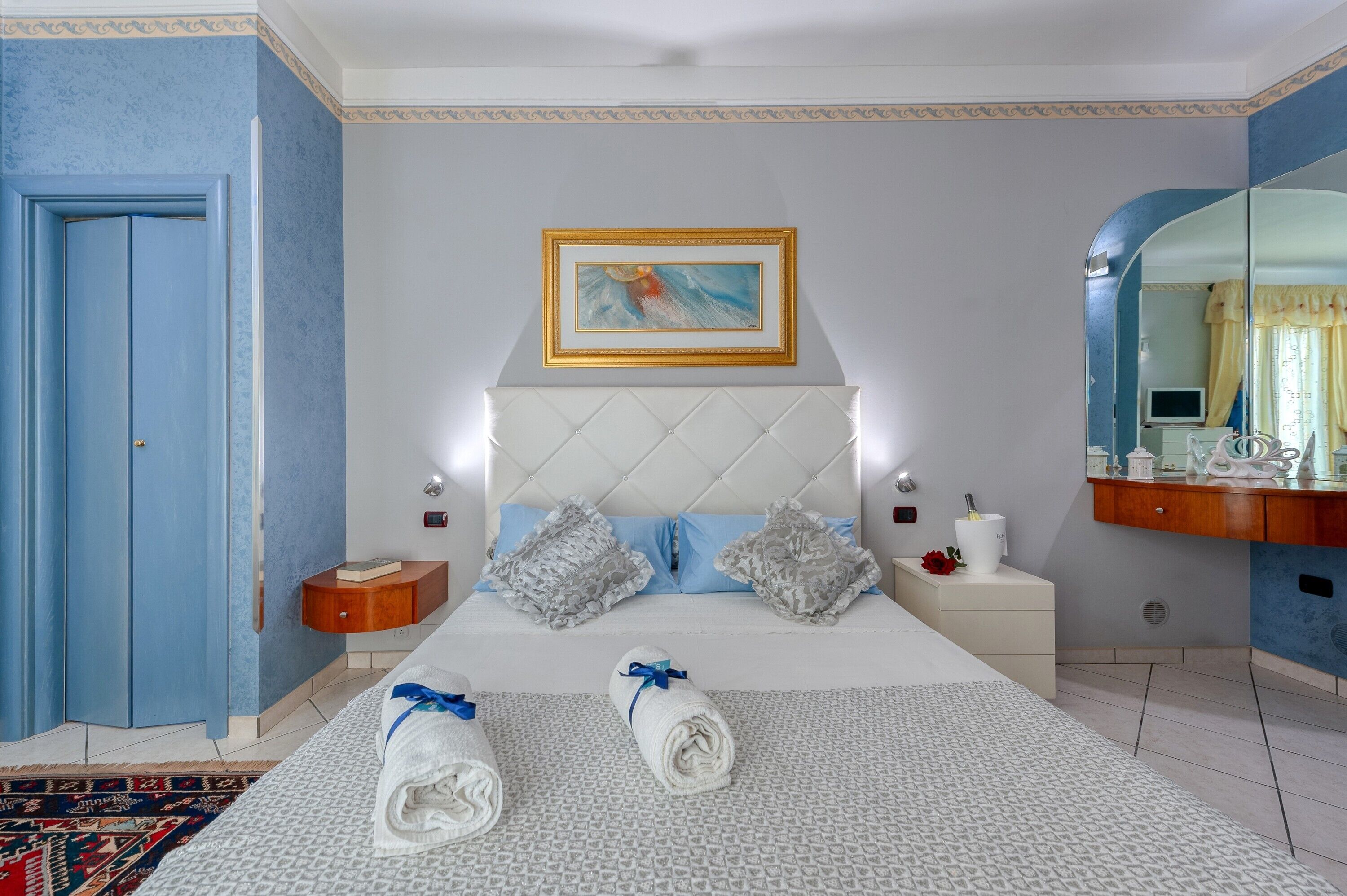 Une chambre à coucher comprenant un lit, deux tables de chevet, une commode, un miroir et une porte.