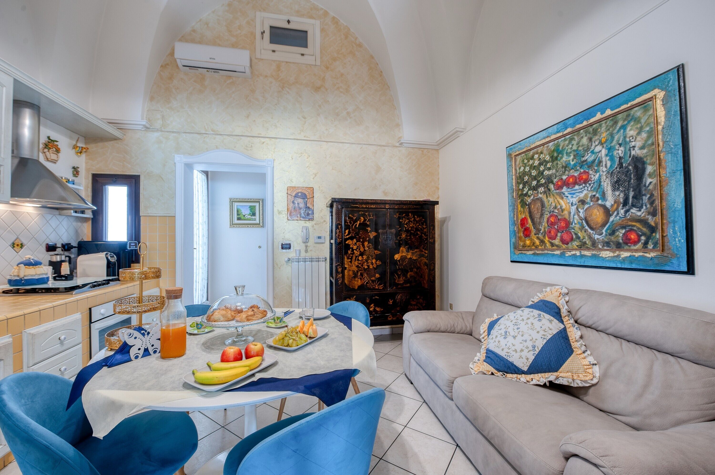 A dining area with a table set for four, a sofa, and a large painting on the wall.