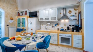 A modern kitchen with white cabinets, a built-in oven, and a dining area with blue chairs.
