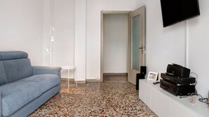 Habitació moderna amb un sofà gris, una taula petita blanca, una televisió de pantalla plana i un moble blanc amb equipament d'àudio.