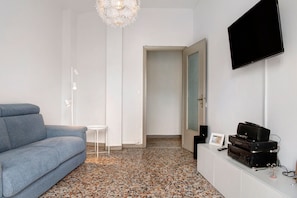 Une pièce moderne avec un canapé gris, une petite table blanche, un téléviseur à écran plat et une console blanche contenant du matériel audio.