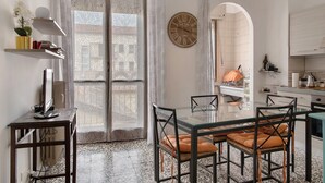 Una cuina moderna amb zona de menjador, un gran finestral amb cortines estampades i un rellotge de paret.