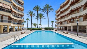 Une piscine à l’eau d’un bleu cristallin, entourée de palmiers et bordée d’un immeuble à plusieurs étages doté de balcons.