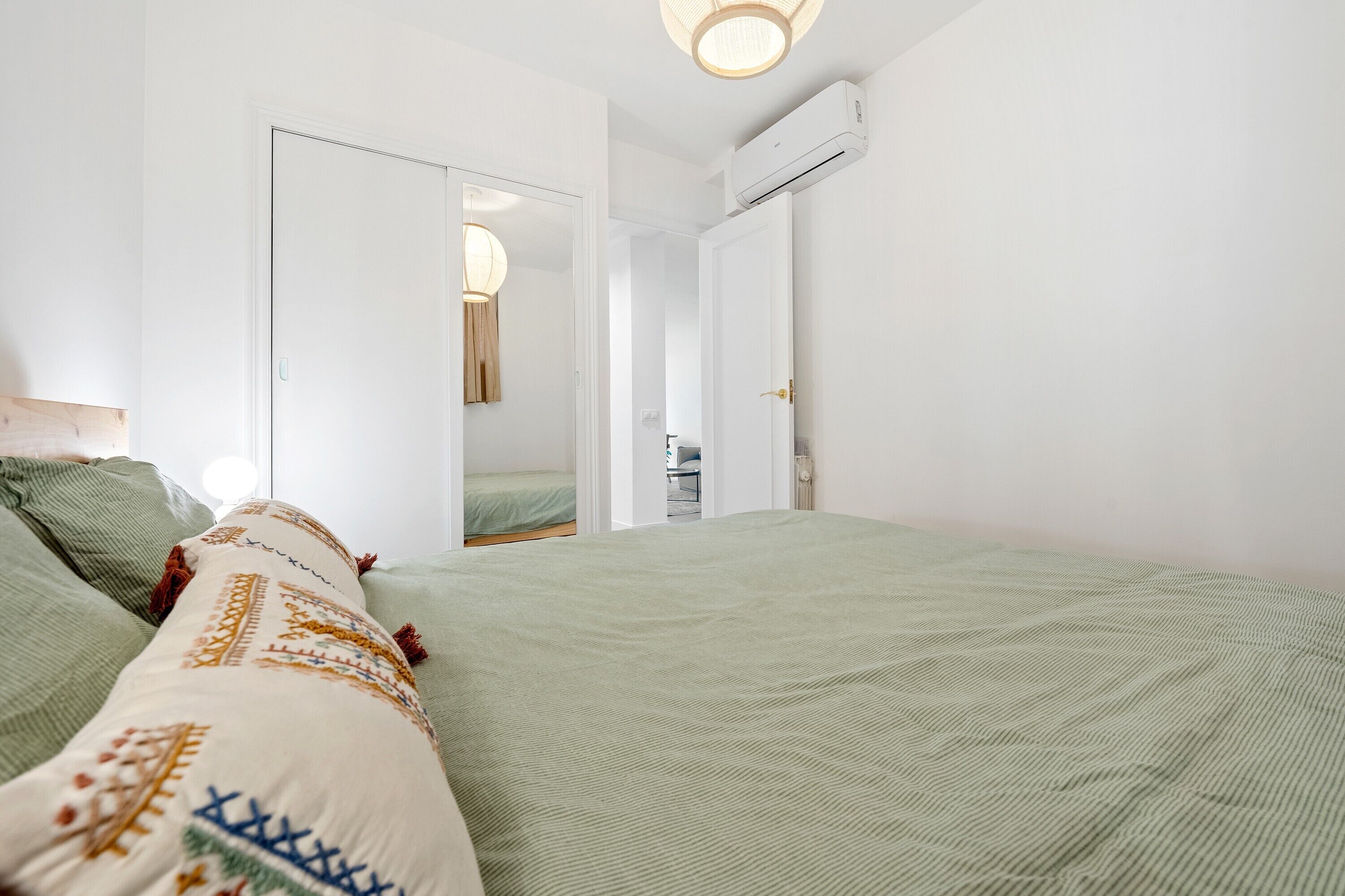 Ein Schlafzimmer mit grüner Bettdecke, einem gemusterten Kissen und einer weißen Wand mit einer Deckenleuchte.