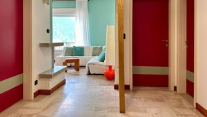 A hallway leading to a room with a red door, a white sofa with green cushions, and a window with white curtains. - Villa 'The Queen Of Garda' with Lake View, Private Garden and Balcony (Riva del Garda)