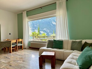 Una sala de estar con un sofá, una mesita, una mesa de comedor con sillas y vistas a montañas a través de un ventanal grande.