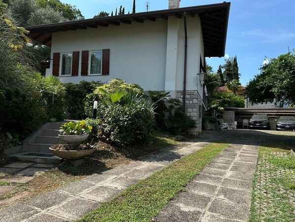 Una casa con entrada pavimentada, jardín con una maceta grande y garaje con dos coches.