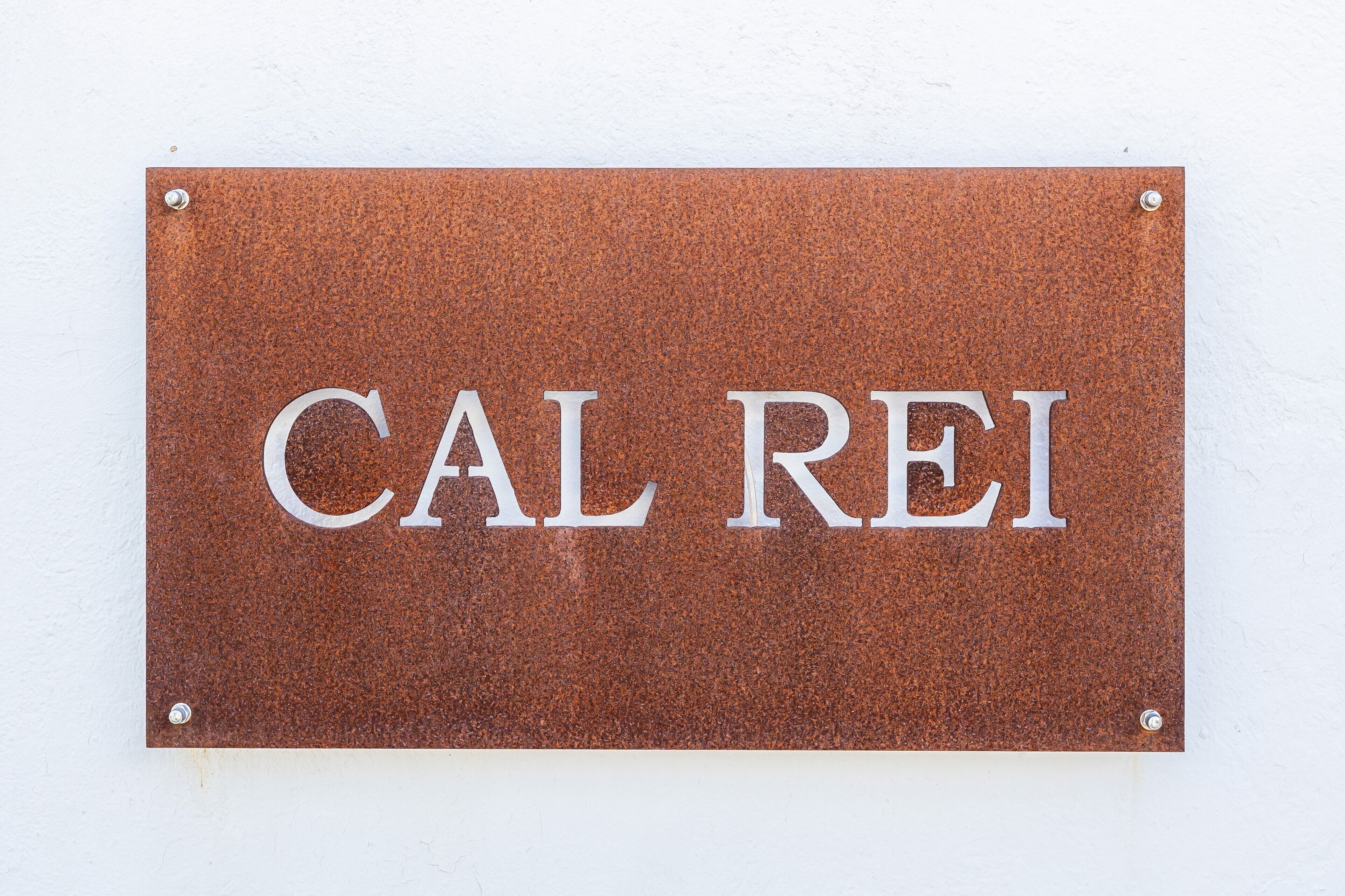 A rectangular sign with the text 'CAL REI' mounted on a white wall.