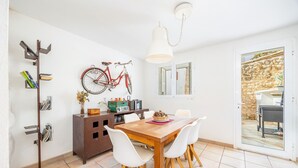 A dining area with a wooden table, white chairs, a red bicycle, a white pendant light, and a stone wall visible through a glass door. - Holiday Home 'Cal Rei' with Private Pool, Wi-Fi and Air Conditioning (Inca)