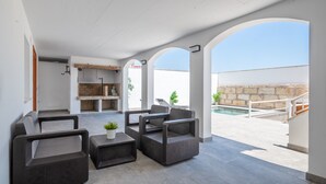 Eine Terrasse im Freien mit Korbmöbeln, einem Pool und einer Steinmauer.