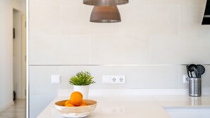 Eine moderne Küche mit weißer Arbeitsplatte, einer Obstschale, einem Blumentopf und einer Hängeleuchte.