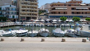 Ein Yachthafen mit vor Anker liegenden Booten, eine Uferpromenade und mehrstöckige Gebäude im Hintergrund.