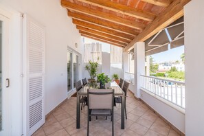 A covered balcony with a dining table, chairs, potted plants, and a view of the city.