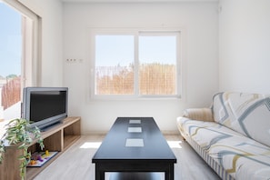A living room with a TV on a wooden stand, a sofa, a coffee table, and a large window with a view.