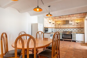 A dining area with a round wooden table and chairs, a kitchen with a brick backsplash, and a white refrigerator.