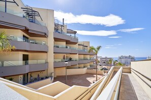 A multi-story residential building with balconies, a clear sky, and a distant view of the sea. - Apartment 'Vacaciones En La Costa Del Sol A114' with Sea View, Pool & Air Conditioning (El Morche)