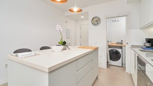 Eine moderne Küche mit einer zentralen Kochinsel, Pendelleuchten, einer Waschmaschine und einer Wanduhr.