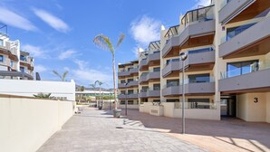 Ein moderner Wohnkomplex mit mehreren Balkonen, einem gepflasterten Innenhof und blauem Himmel.