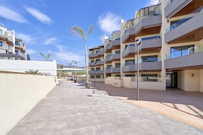 A modern apartment complex with multiple balconies, a paved courtyard, and a clear blue sky.