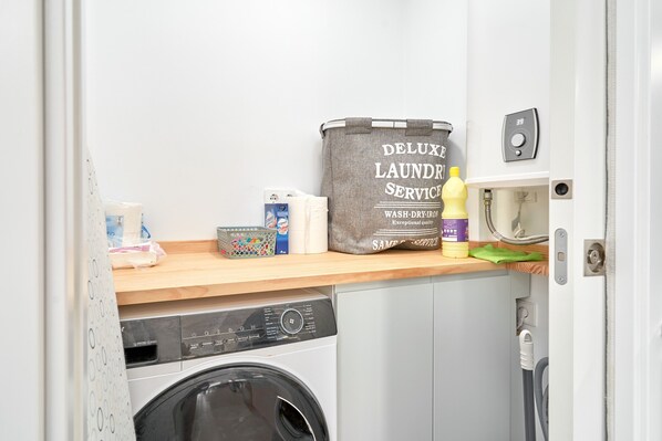 A laundry area with a washing machine, a dryer, and a shelf with laundry supplies. - Apartment 'Vacaciones En La Costa Del Sol A114' with Sea View, Pool & Air Conditioning (El Morche)