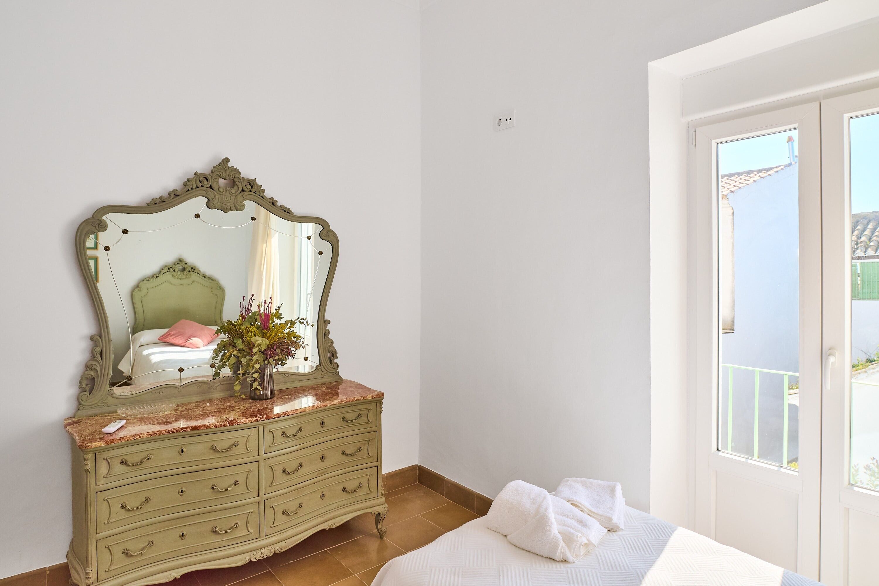 A bedroom with a bed, dresser, mirror, and a window with a view.