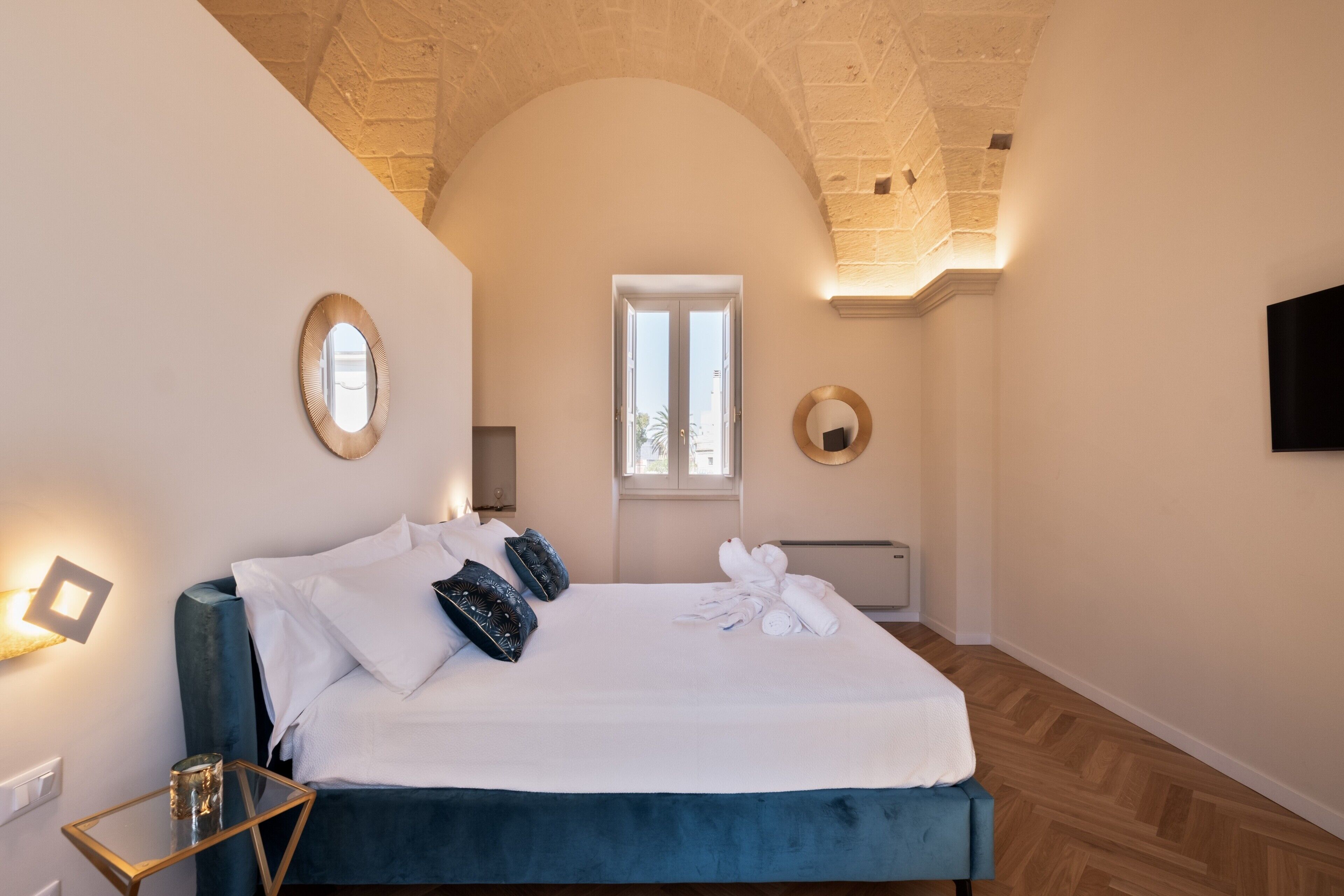 A bedroom with a bed, a mirror, a window, and a wall-mounted TV.