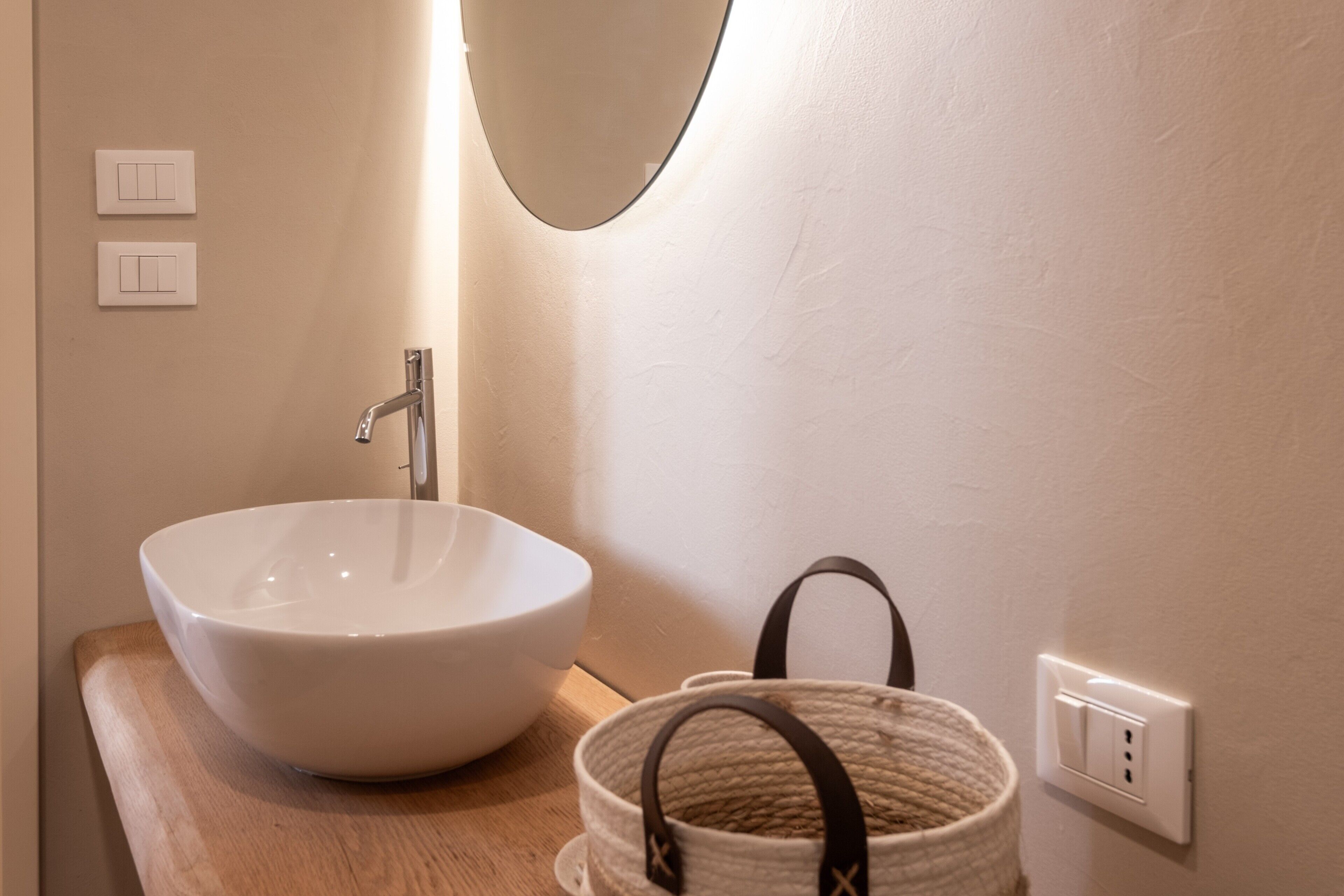 Een badkamer met een witte wasbak, een spiegel en een gevlochten mand.