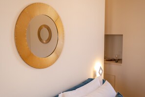 Une pièce avec un grand miroir rond au mur, un lit avec une literie blanche et bleue, et une table de chevet avec une lampe.