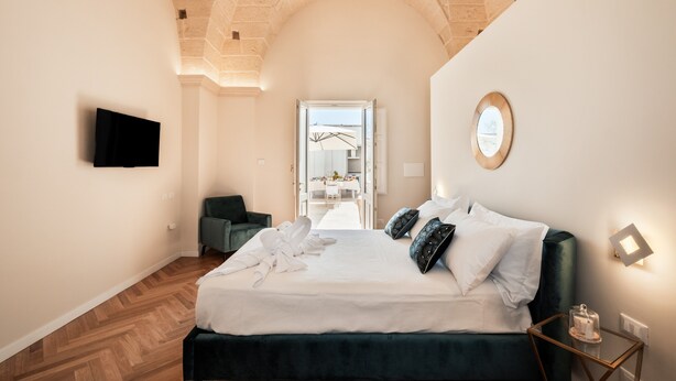 A bedroom with a bed, a television, a chair, and a view of a dining area. - Room 'Relais Luxury Xenia - Ulivo' with Shared Pool, Wi-Fi and Air Conditioning (Sternatia)