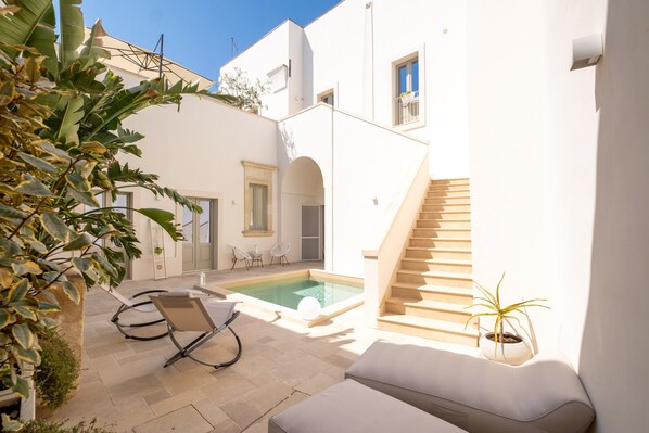 A white building with a pool, a staircase, and outdoor seating.